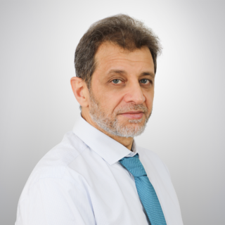 Man in a light blue striped shirt and teal tie, posed against a light gray gradient background.