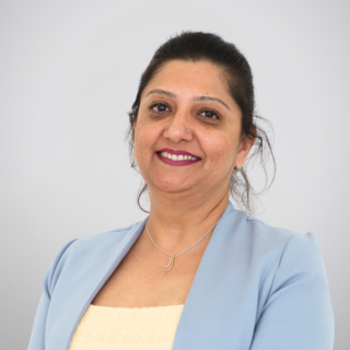 Smiling woman in a light blue blazer posing for a professional portrait against a neutral gray gradient background.
