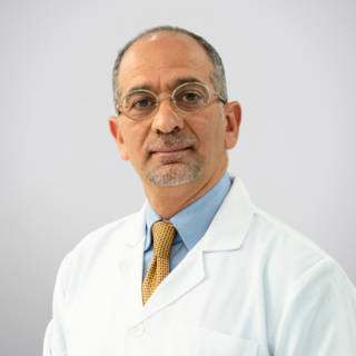 Portrait of a middle-aged doctor wearing a white coat, blue shirt, yellow tie, and glasses.