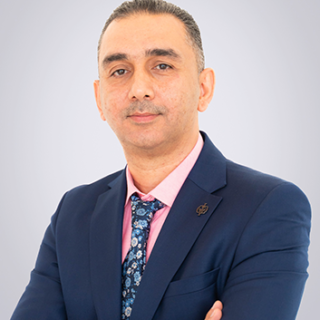 Formal business portrait of a man in a navy suit, pink shirt, and patterned tie, arms crossed.
