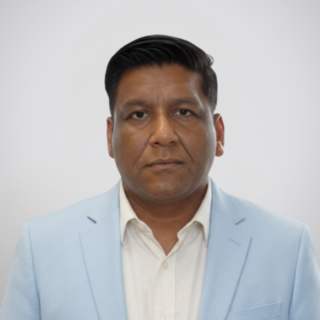 Portrait of a man facing the camera in a light blue blazer and white shirt against a gray gradient background, neutral expression.